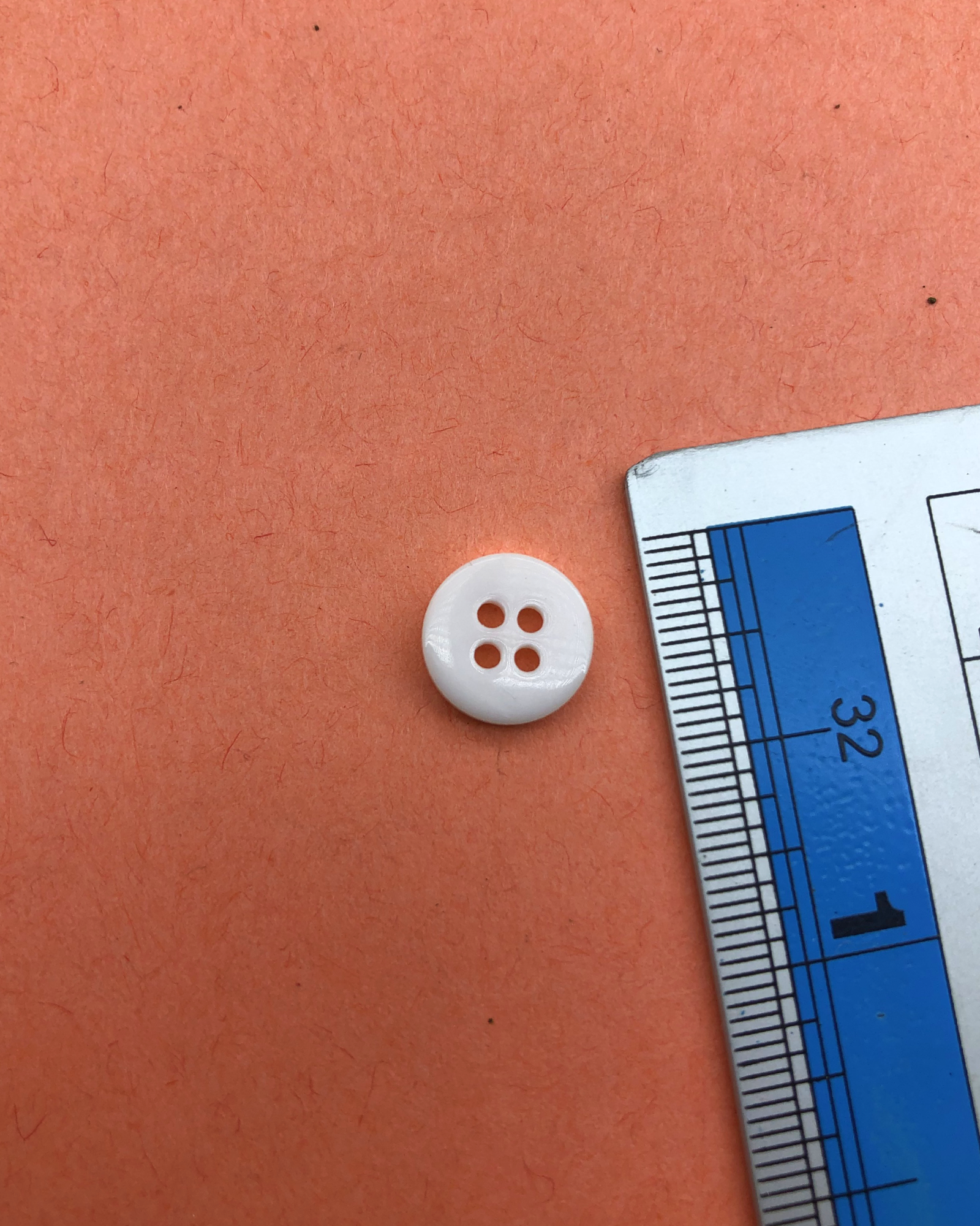 The size of the Beautifully designed 'Four Hole Plastic Button PB002' is measured by using a ruler